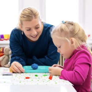 Toddler girl in child therapy session doing sensory playful exercises with her therapist.